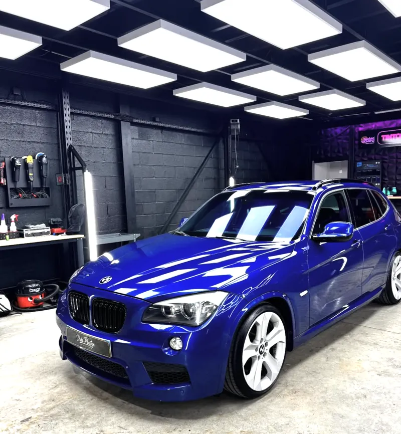 BMW X1 bleue lustrée dans un studio sombre éclairé par des dalles lumineuses