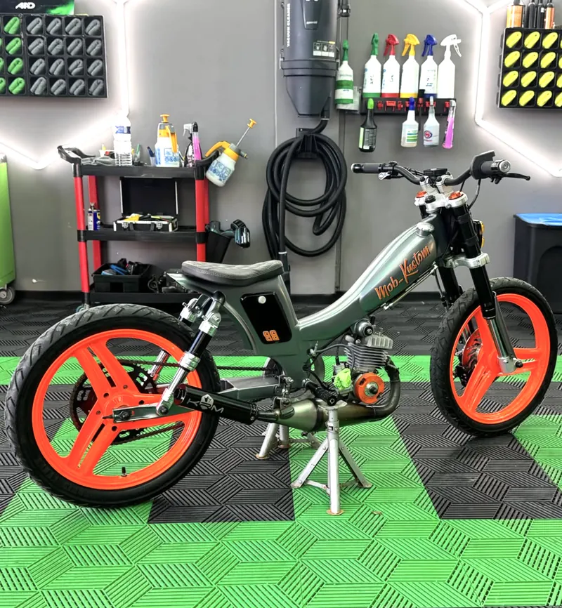 Mobylette custom aux jantes orange, nettoyée en profondeur, devant un mur de produits de detailing