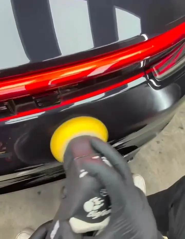 Polisseuse à mousse jaune sur le bandeau arrière d'une Porsche 992, tenue par des mains gantées