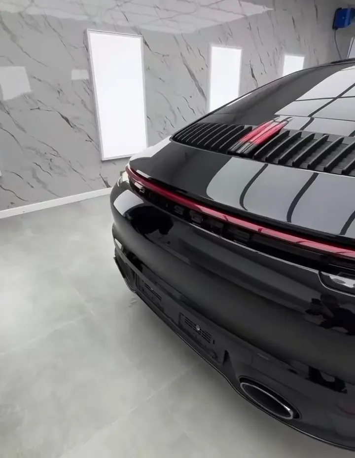 Porsche 992 noire vue de l'arrière dans un studio blanc, la peinture miroir reflétant le plafond lumineux